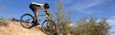 A rider descending a rocky desert trail against a blue sky